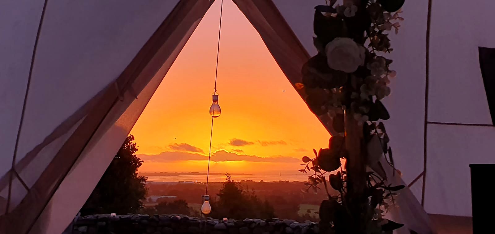 Wide view of the sunset from inside the tent, greenery at the doorway