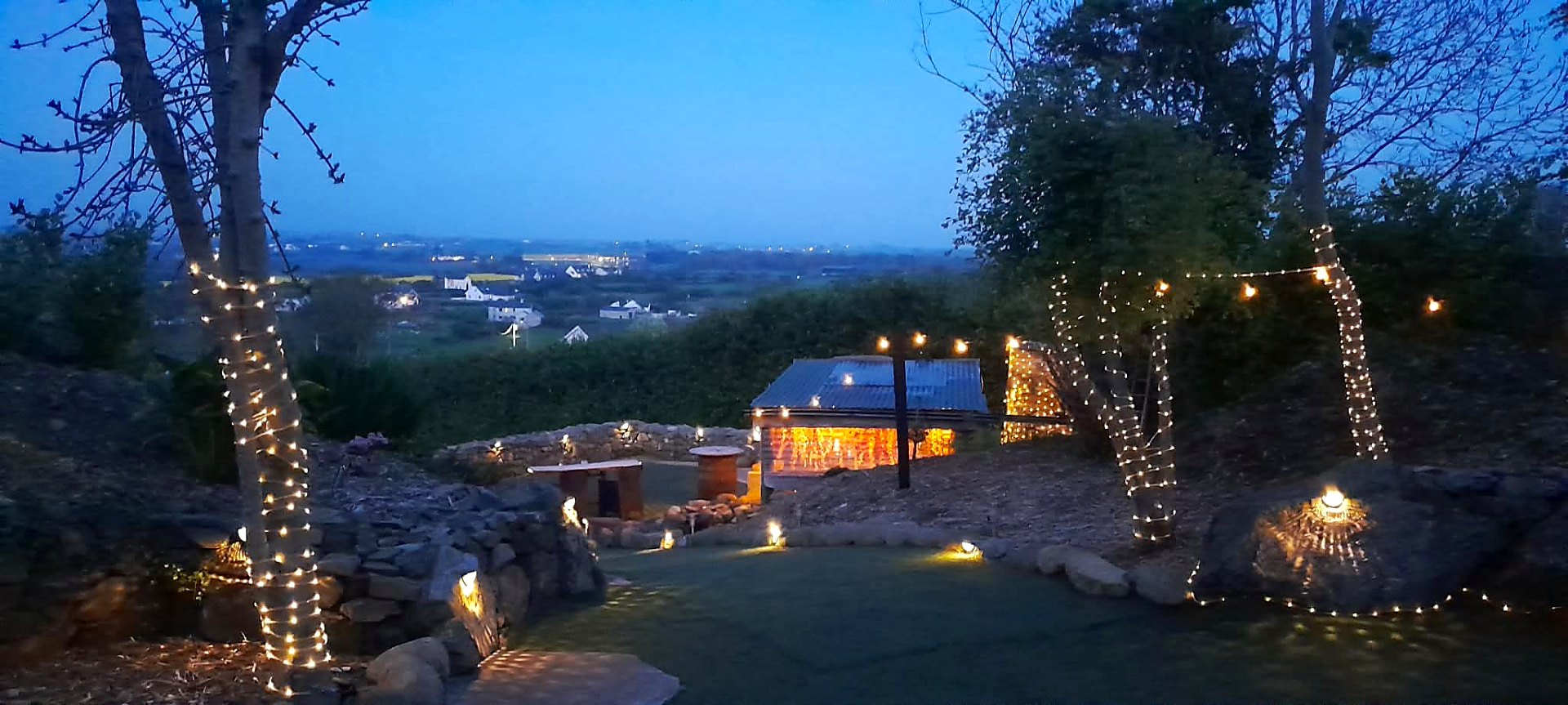 Trees wrapped in fairy lights above the lawn at Fairy Cove as the light fades