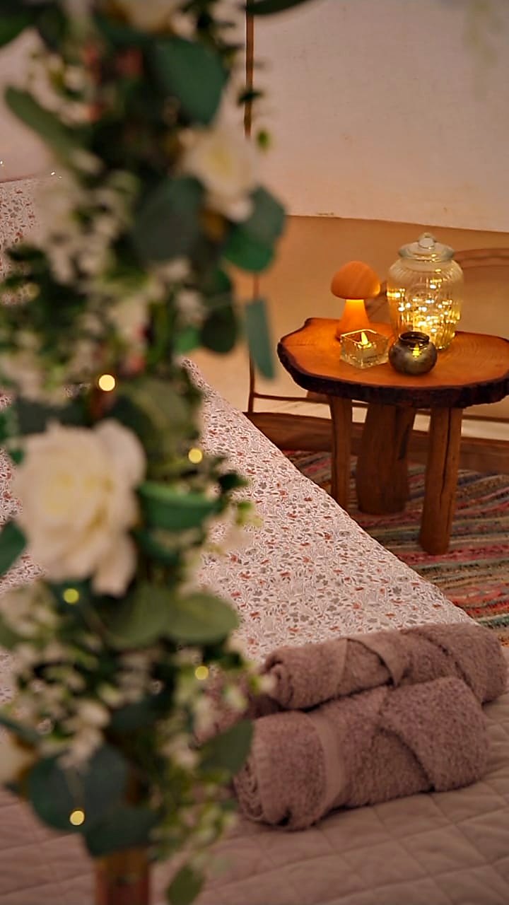 Rolled towels on the bed beside a live-edge table with candles and a jar light