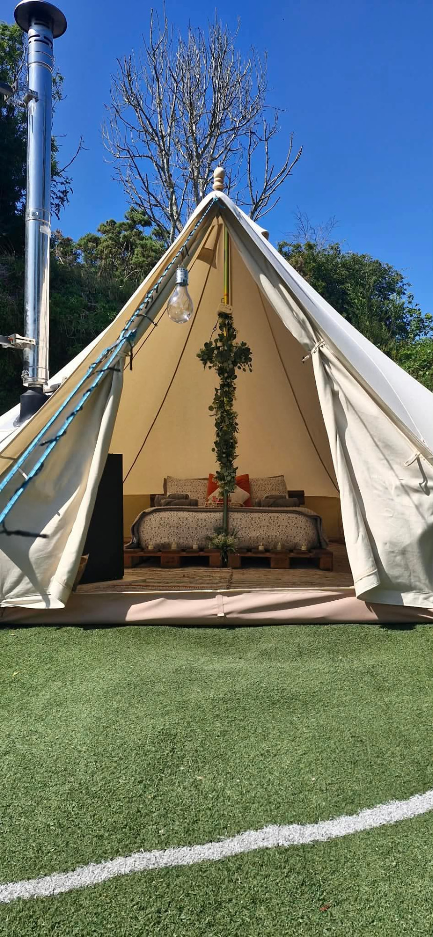 Fairy Cove bell tent open to the lawn on a bright day, its stove flue rising beside the canvas