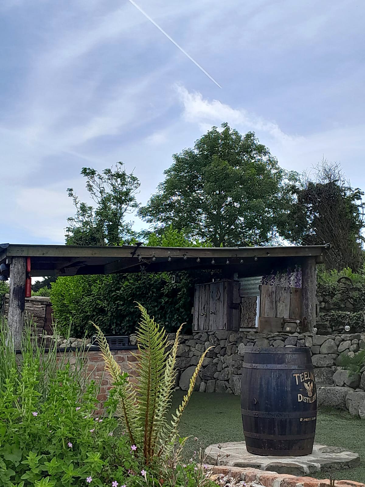 The covered cooking shelter at Fairy Fort by day, with ferns, stone walls and an old barrel