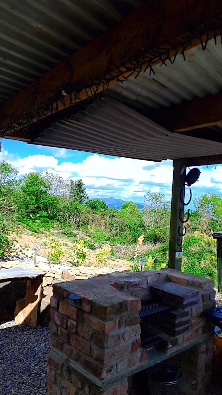 Fairy Hill's covered outdoor kitchen with brick barbecue, looking out over trees and fields to the coast