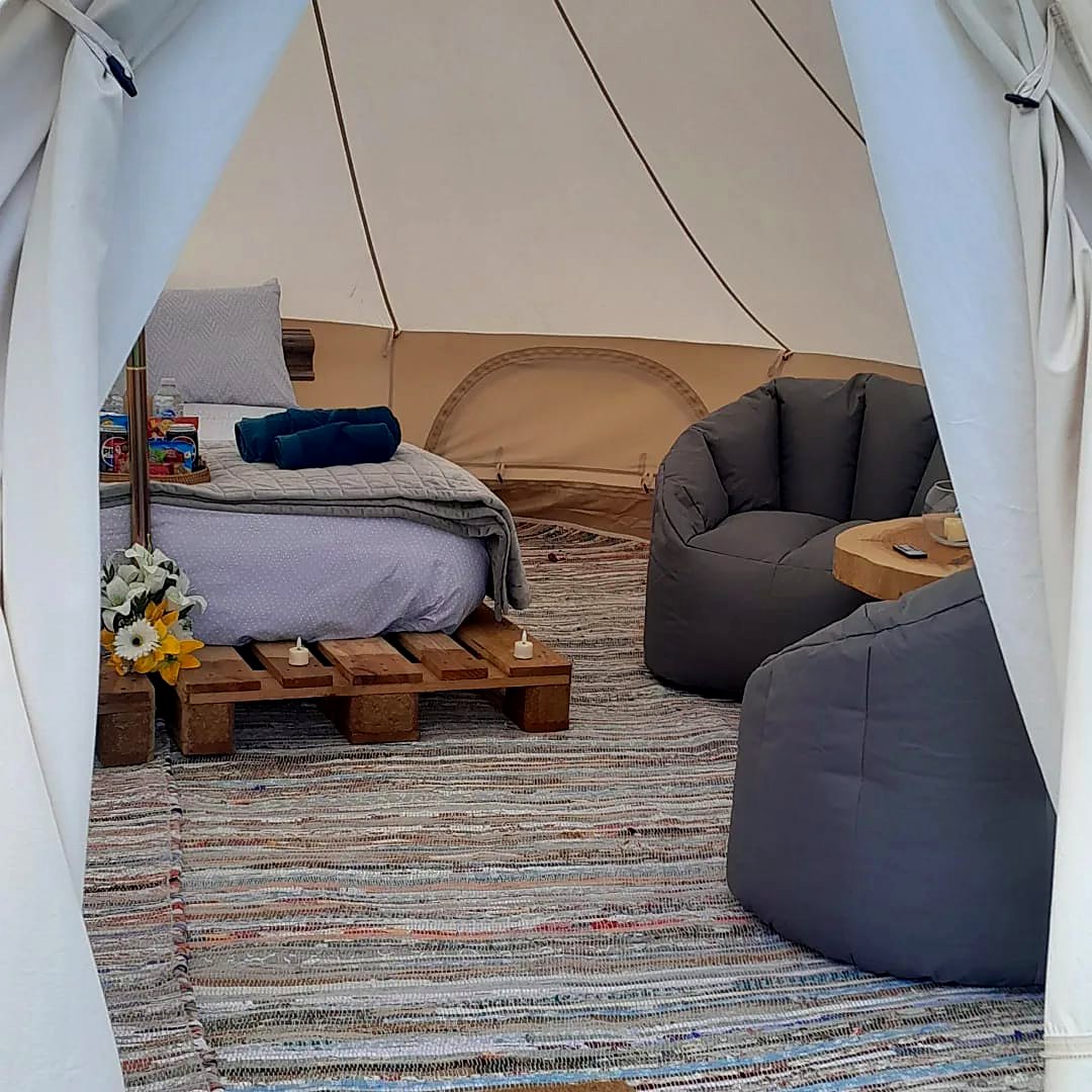 Inside Fairy Hill — a made-up double bed, soft seating and a woven rug beneath the canvas